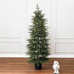4ft christmas tree stands on wooden floor next to white plush owl, white paneled wall in the background.