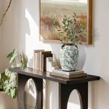 A decorative console table with books, white bookends, and a round floral ceramic vase with foliage.