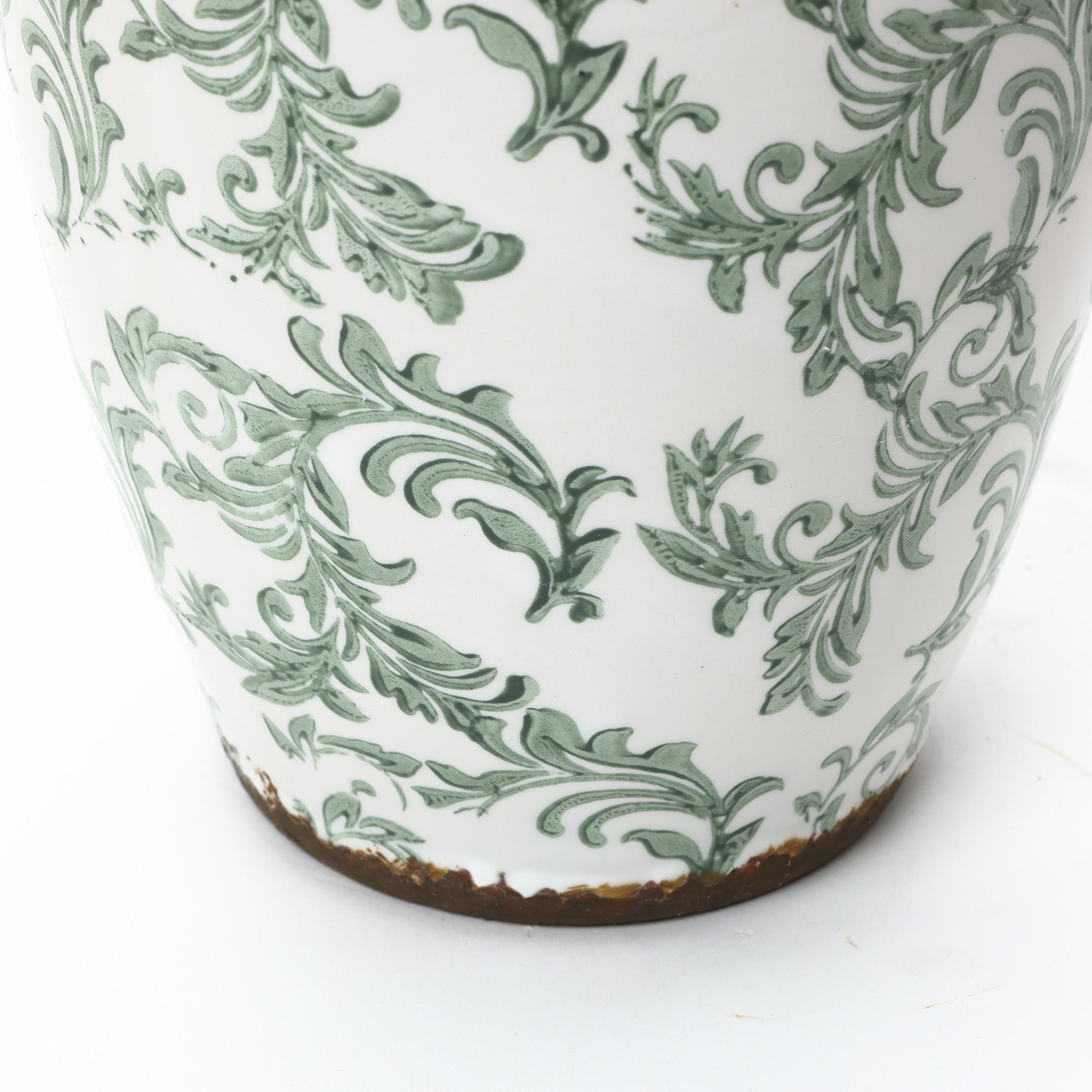 Close-up of a round floral ceramic vase, showcasing green ornate patterns and a chipped, brown-stained base.
