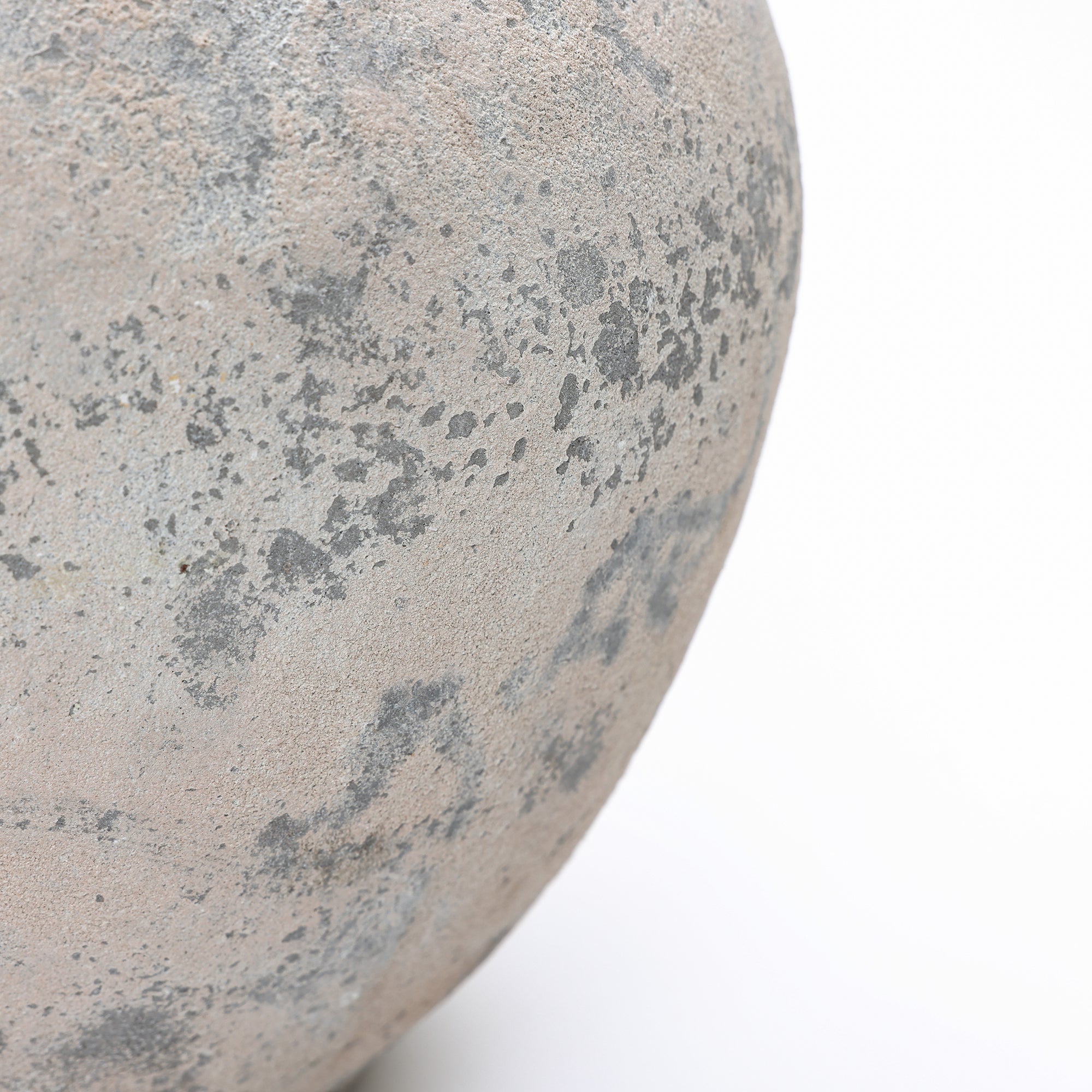 A close-up view of a textured, grayish-brown stone surface with scattered dark speckles against.
