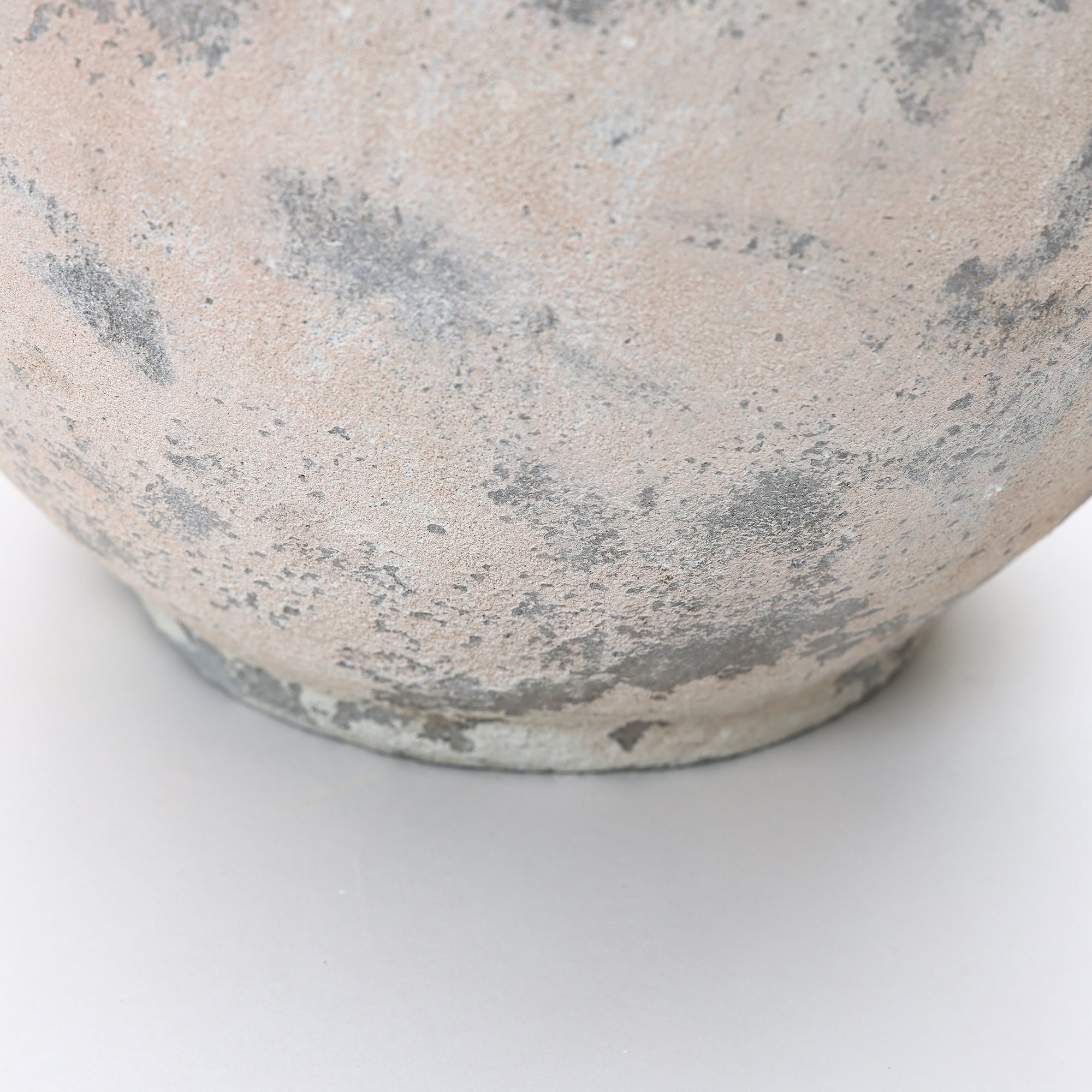 Close-up of the bottom portion of a textured, weathered with gray and beige tones, sitting on a light surface.