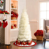 Slim pampas grass tree with wrapped gifts underneath stands in living room with red accents natural light.
