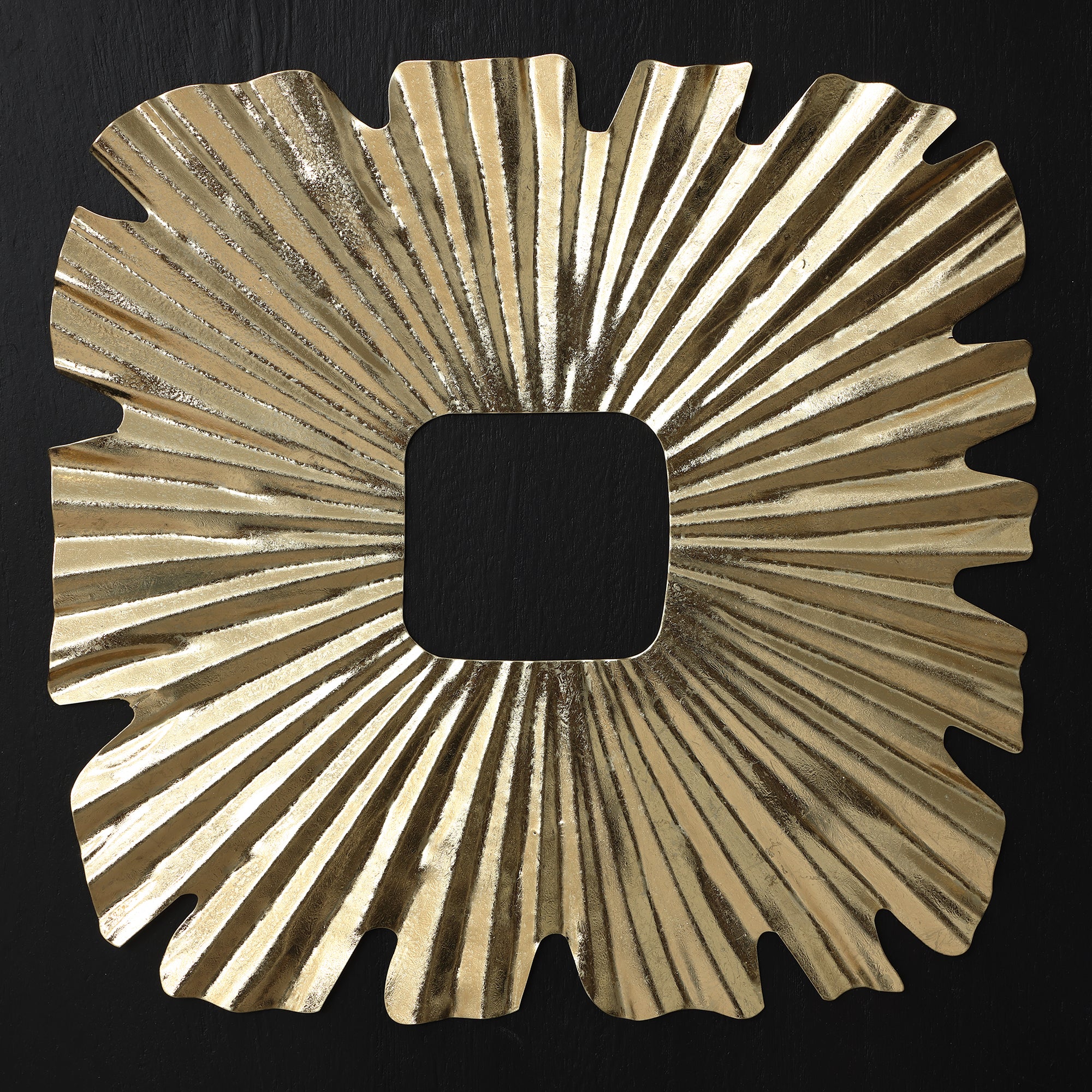 Square gold-toned sunburst wall art piece with radiating, textured lines and wavy edges, featuring a central square cutout.