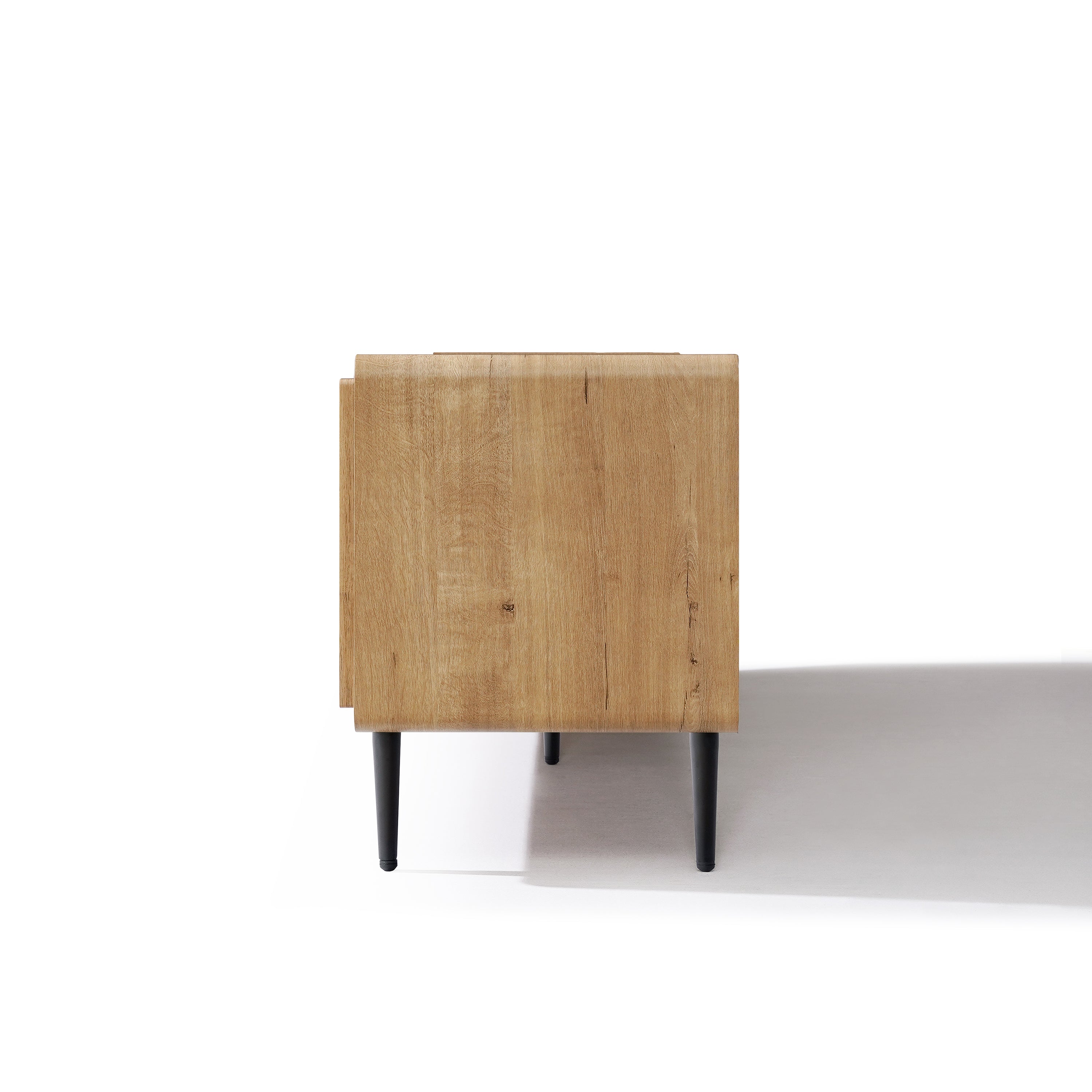 Side view of a wood TV stand with black legs, placed on a white surface with a shadow cast to the right.