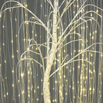 Close-up of artificial willow tree with thin branches, wrapped in small, warm white string lights against gray background.