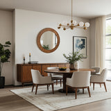 Modern dining room with a wooden table, white chairs, sideboard, oak wood frame round wall mirror, and a gold chandelier.