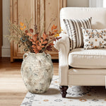 Terracotta Vase with rustic antiqued finish filled with autumn foliage, placed on the floor beside a cream sofa with patterned pillows in a cozy farmhouse living room.