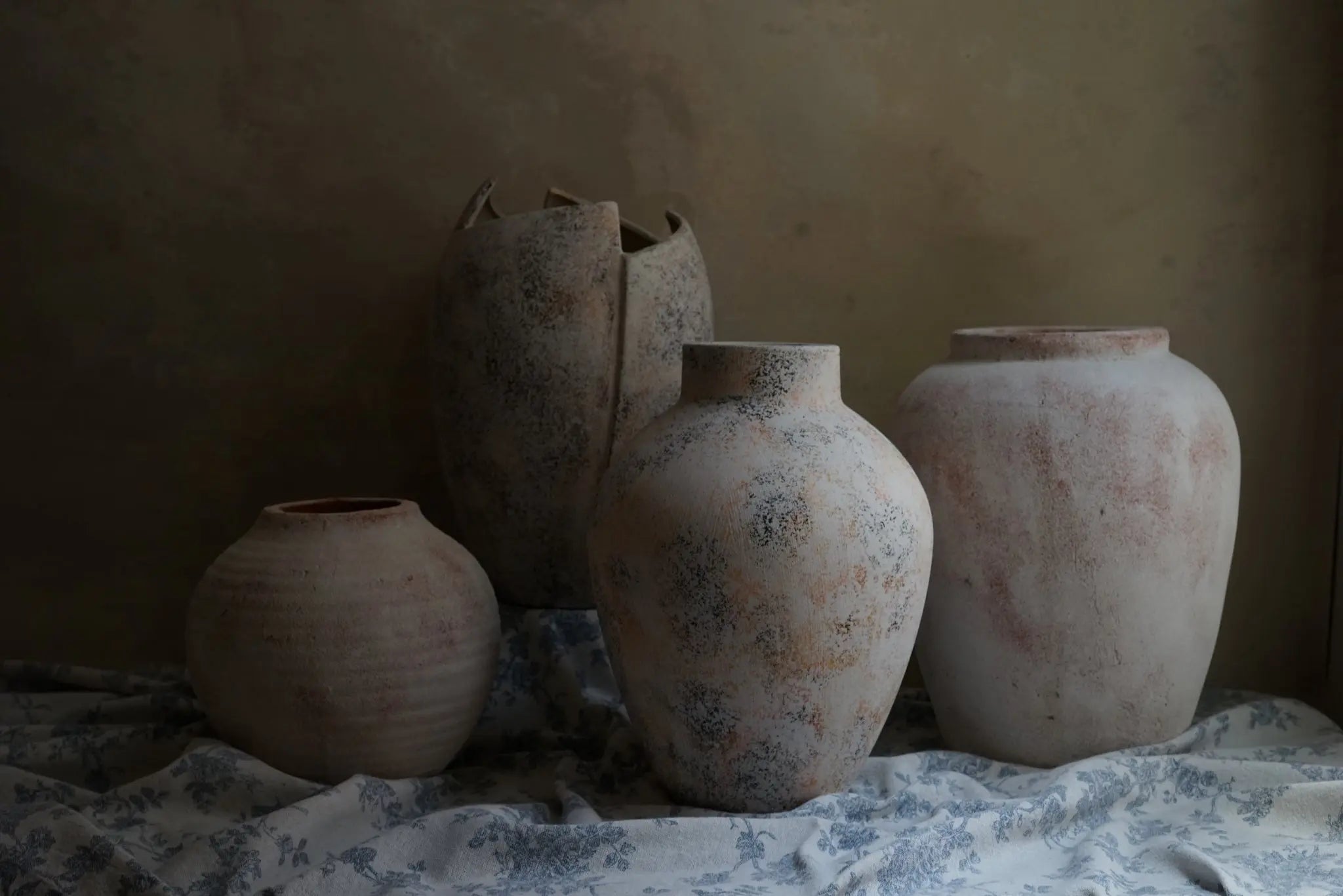 Four textured ceramic vases in varied shapes and sizes are artfully arranged on a patterned cloth, set against a muted background. These exquisite pieces of home decor boast subtle white marble textures that enhance their elegant charm.