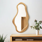An irregularly shaped mirror with a pine frame hangs on a wall above a wooden console, infusing the space with natural energy. A potted plant with green and brown leaves sits on the console, enhancing the organic decor.