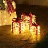 Three lighted gift boxes with red bows are displayed on a stone patio next to a lit snowman figure, creating charming holiday decorations.