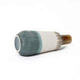 A high-quality ceramic vase on its side showcases a ribbed texture, featuring a color gradient from gray-blue to white and brown, making it an exquisite piece for home decor.
