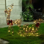 Wireframe Reindeer and Sleigh holiday decoration with LED lights and red bows are displayed on a grassy lawn beside a house.