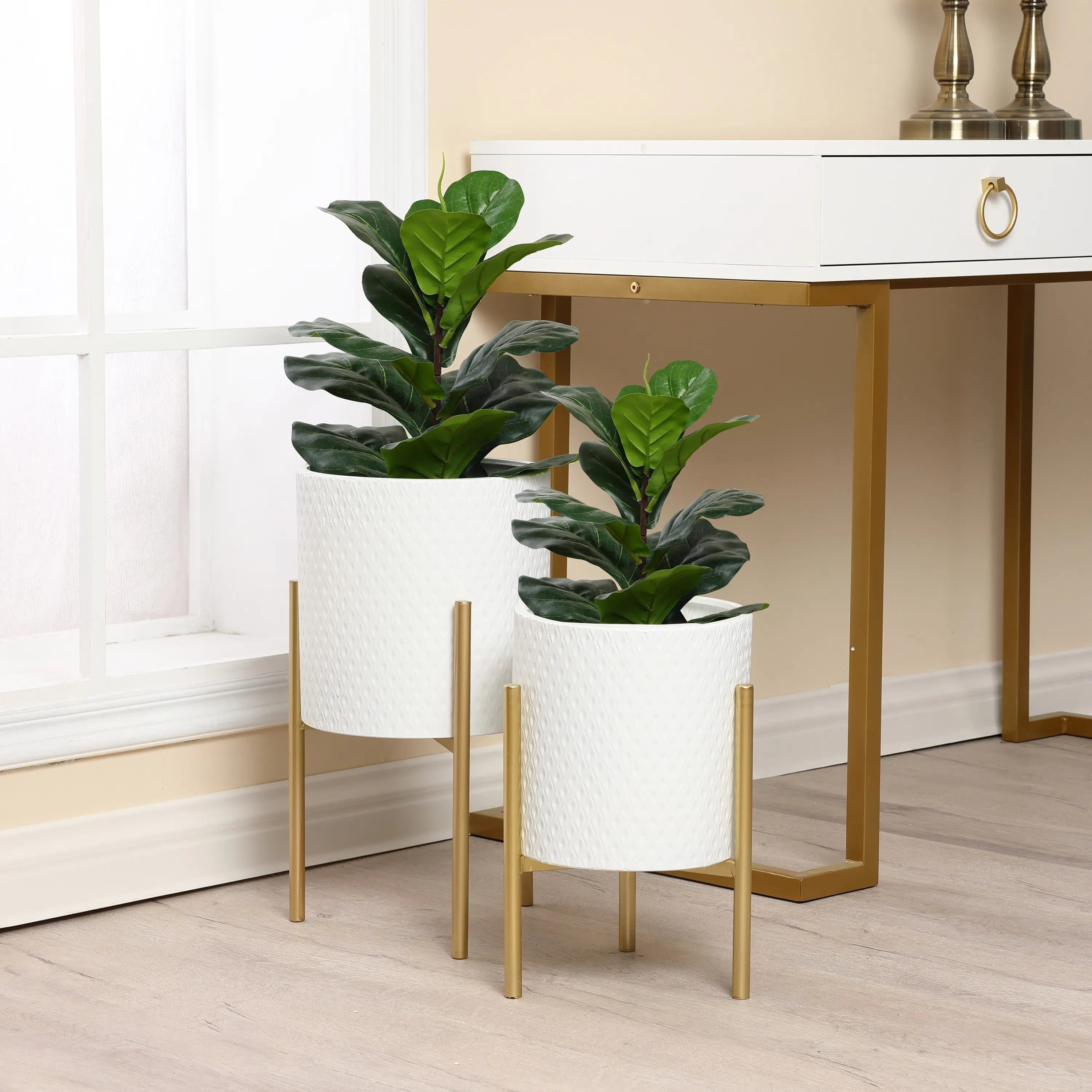 Two green potted plants in white metal planters with gold stands add minimalist design flair next to a modern white and gold desk.