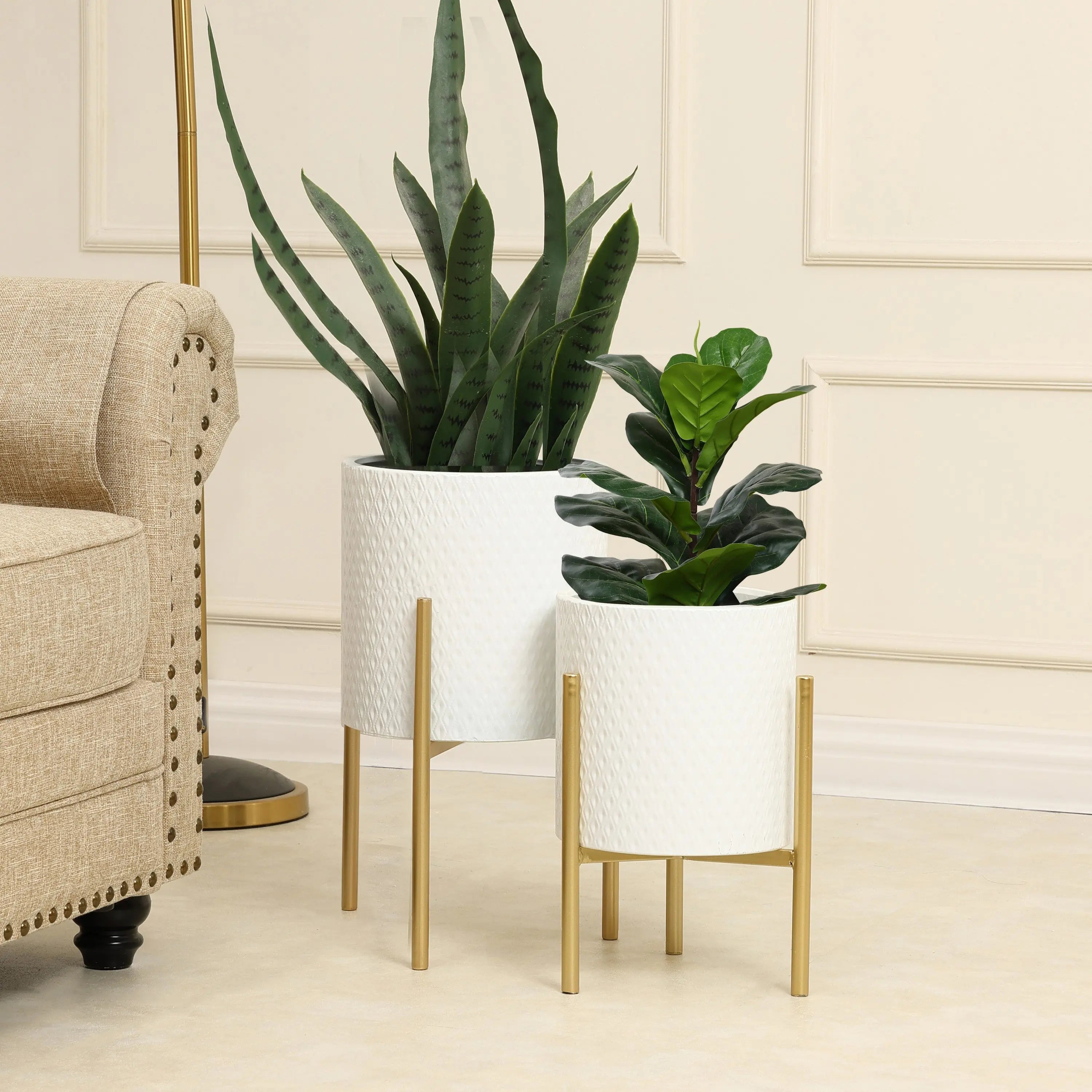 Two potted plants in white metal planters with gold stands add a touch of contemporary modern style next to a beige upholstered sofa in the living room.