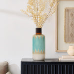 A coastal-inspired vase with a blue and beige gradient design holds dried branches, adding nautical charm to the dark wooden cabinet near a framed artwork.