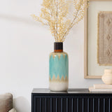 A coastal-inspired vase with a blue and beige gradient design holds dried branches, adding nautical charm to the dark wooden cabinet near a framed artwork.