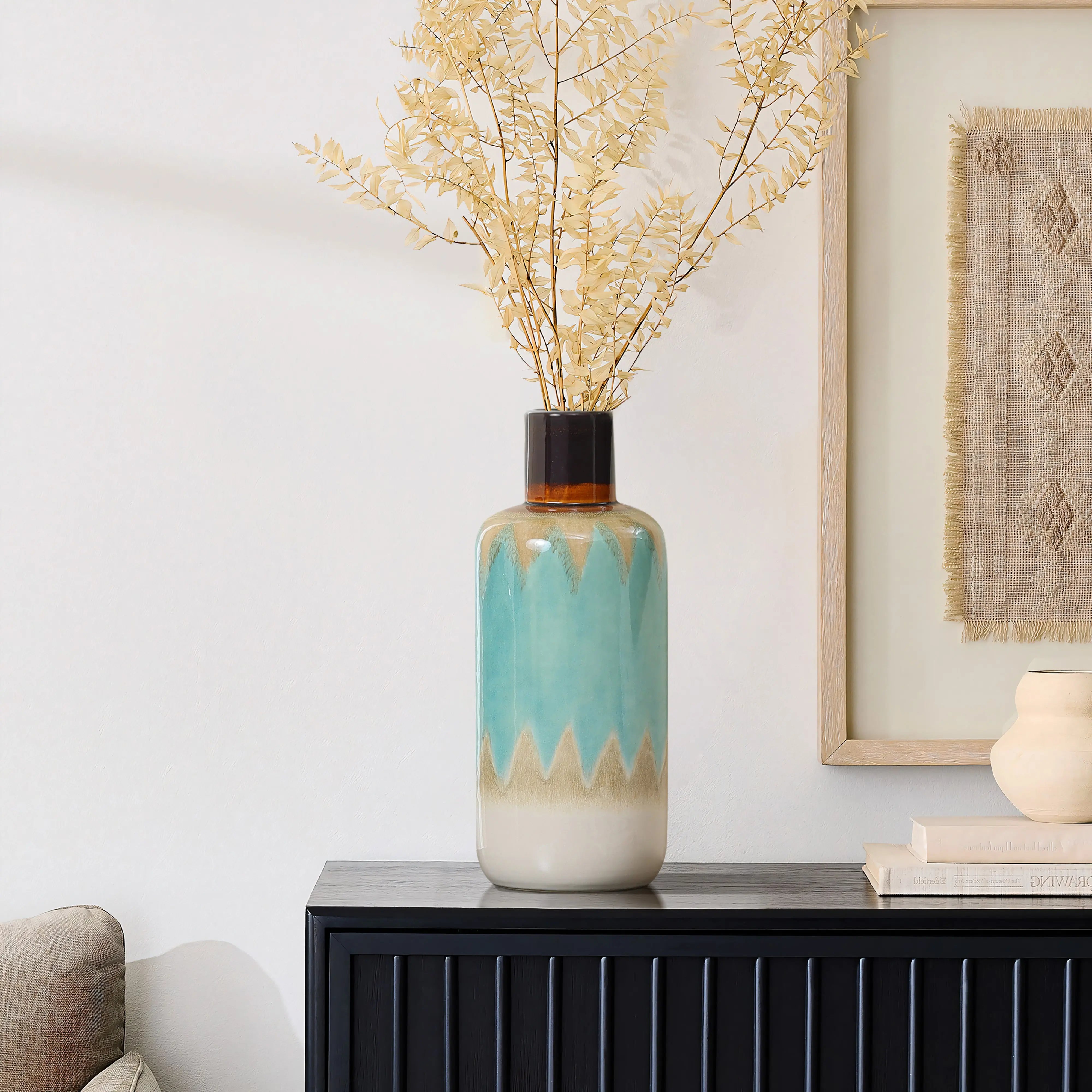 A coastal-inspired vase with a blue and beige gradient design holds dried branches, adding nautical charm to the dark wooden cabinet near a framed artwork.