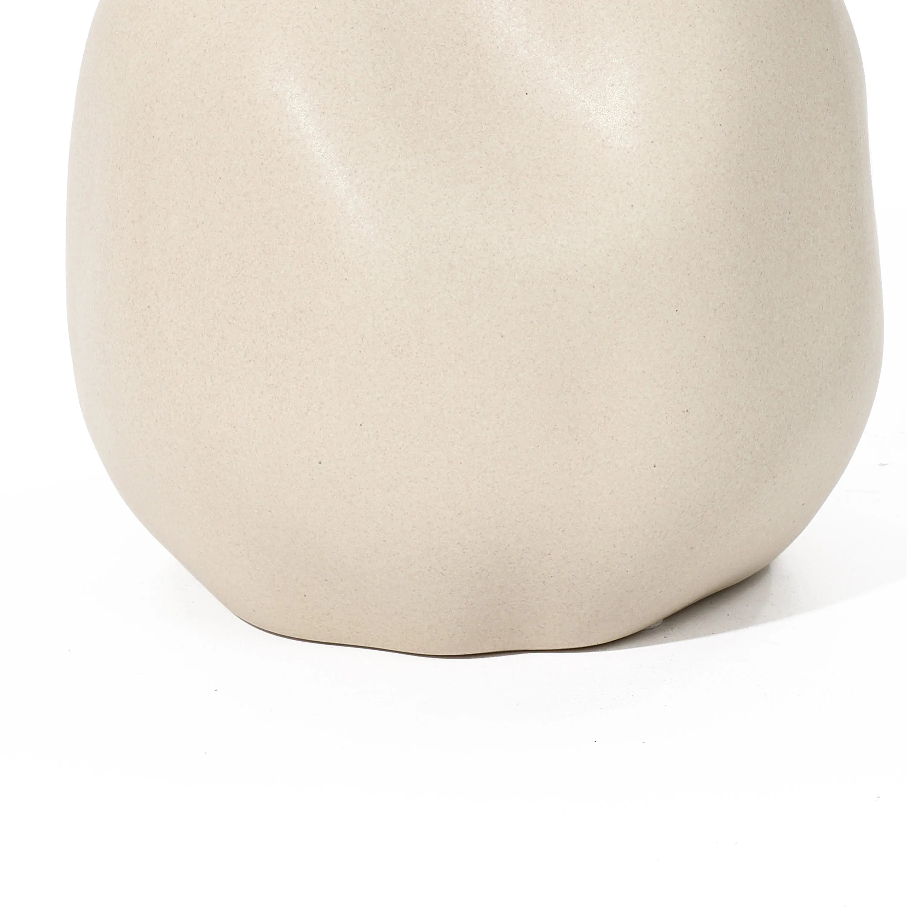 A smooth, matte beige ceramic vase with an irregular, rounded shape serves as a stunning accent piece against the ivory white background.