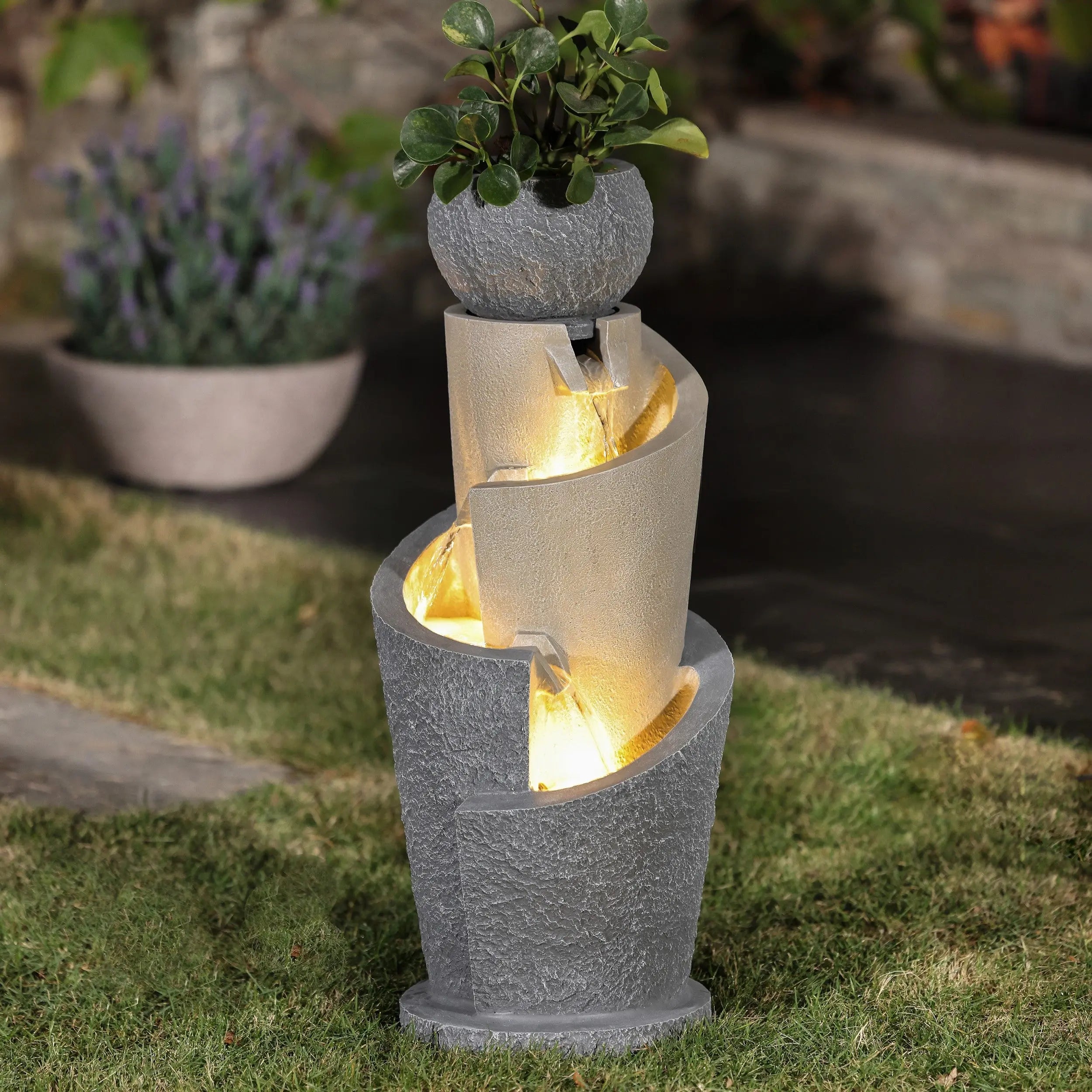 A flower pot water fountain with LED lights, featuring three concrete-like basins and a small potted plant on top, adds charm to garden spaces when placed on a grassy lawn.