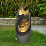 Modern patio fountain with a sculptural, cascading curved structure stands on green grass, featuring two water basins and a textured surface, with plants and a stone wall in the background.