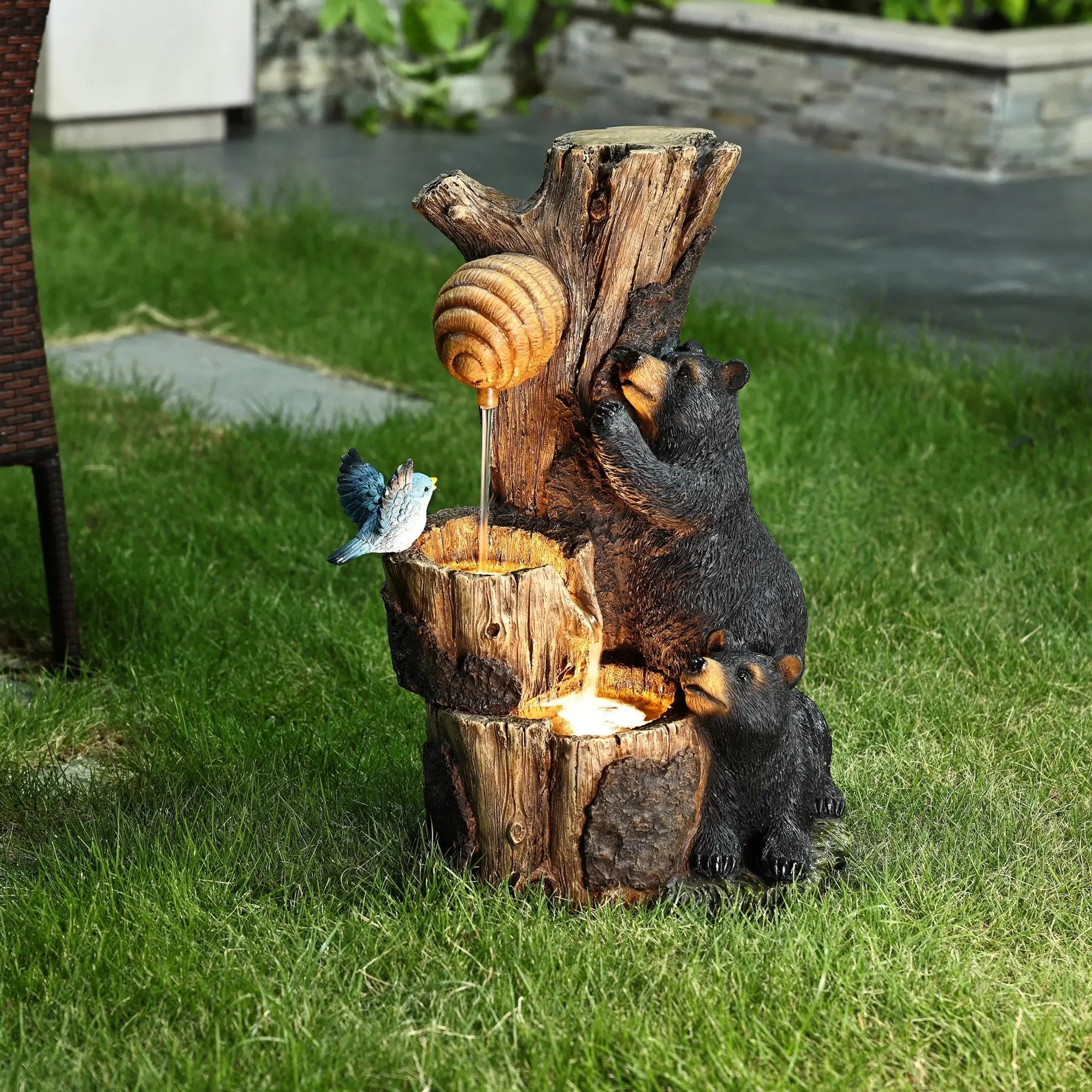A decorative bear outdoor fountain shaped like a tree stump, featuring two bears, a beehive, and a bird with water flowing into a lit basin—crafted from durable resin for your garden or patio.
