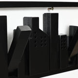 Black abstract cityscape sculpture, crafted from solid fir wood, mounted on a white wall with a visible screw.