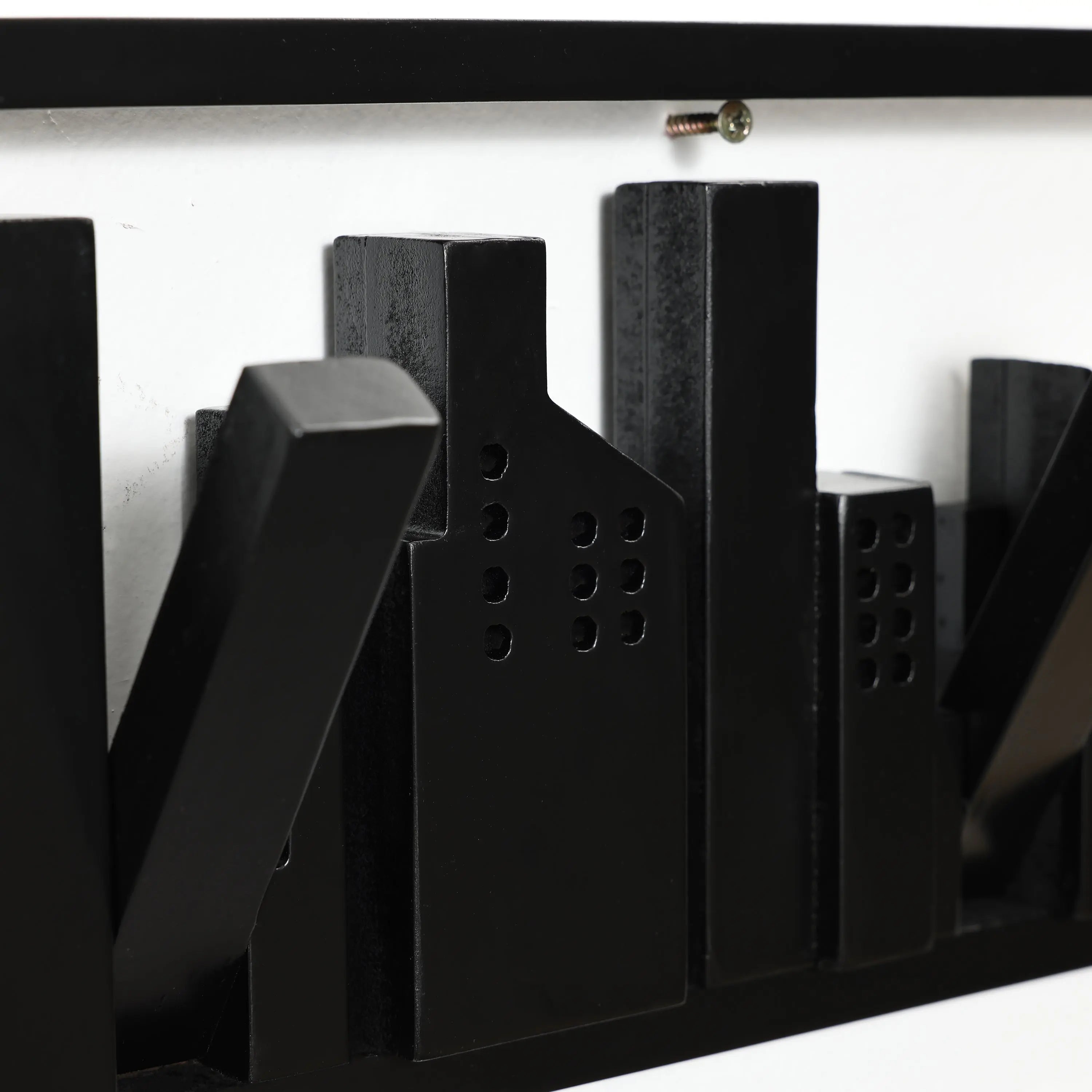 Black abstract cityscape sculpture, crafted from solid fir wood, mounted on a white wall with a visible screw.