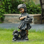 Whimsical statue: Bronze-colored girl with a basket of flowers stands beside a small dog on the grass. A stone wall and lush greenery form the backdrop, making this weather-resistant piece a charming addition to garden statues.