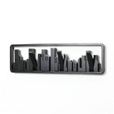 A black metal wall sculpture depicts a minimalist cityscape silhouette against a white background, seamlessly integrated with a solid fir wood wall-mounted coat rack featuring convenient flip-down hooks.