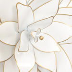 Close-up of a white decorative flower with gold-edged petals and a gold center, capturing the essence of metallic art.