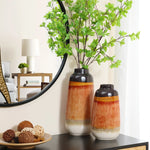 Two vintage ceramic vases with green branches sit elegantly on a table next to a round mirror. A lamp and small plant accentuate the home decor, adding charm and character to the background.