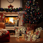 A decorated living room with a lit fireplace, Christmas tree, stockings, and illuminated reindeer and sleigh LED lights creating a festive holiday decoration in front of the tree.