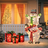 Two lighted snowman decorations from the Lighted Snowman Set stand stacked beside three illuminated gift boxes on a snowy porch, with a house window glowing in the background—perfect outdoor holiday decorations.