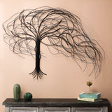 A handcrafted metal tree wall decor with flowing branches hangs above a wooden console table adorned with decorative objects, books, and a glass of wine.