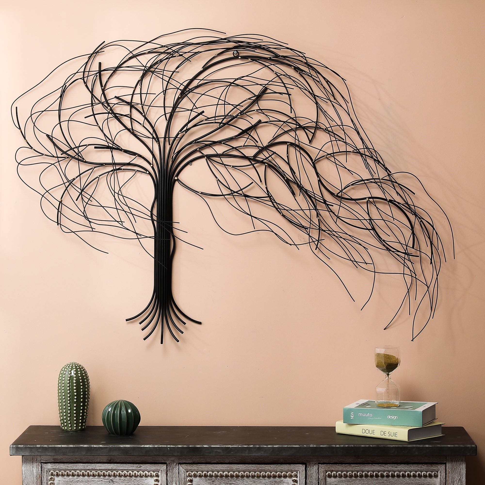A handcrafted metal tree wall decor with flowing branches hangs above a wooden console table adorned with decorative objects, books, and a glass of wine.