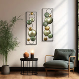 A cozy corner featuring a green armchair, side table, warm lights, and a lush plant is beautifully complemented by two abstract wall decor pieces crafted from metal and tin with circular designs, enhancing the modern setting.