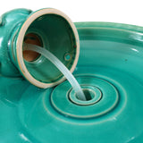 Close-up of water flowing from an open ceramic jug into a wide, shallow turquoise basin with a circular design, creating a decorative garden piece reminiscent of a two-tiered fountain.