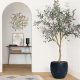 A geometric pot planter made of magnesium oxide material holds a potted plant, resting on a wooden floor beside a decorative wall. Artwork and a small table enhance the backdrop, perfect for indoor and outdoor use.