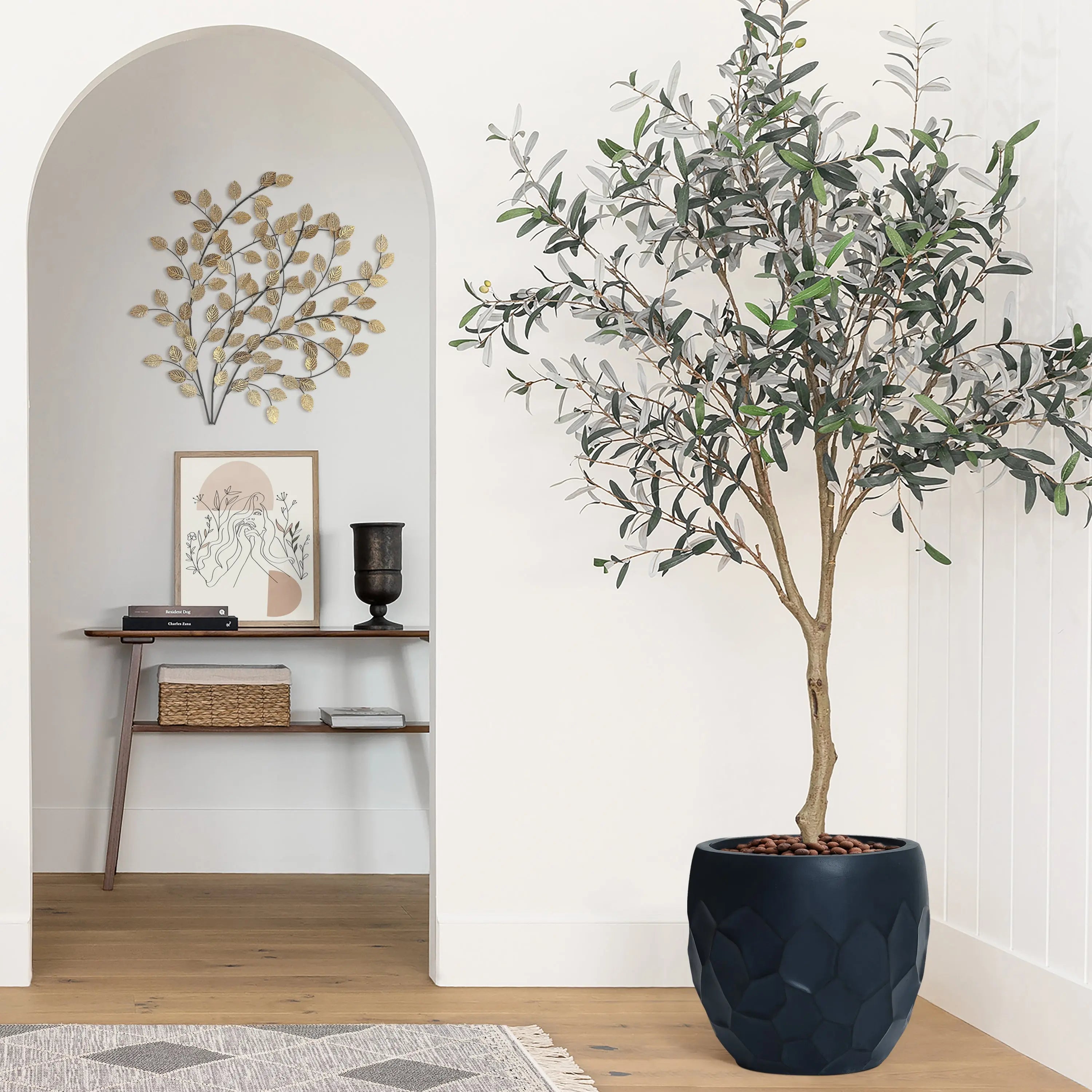 A geometric pot planter made of magnesium oxide material holds a potted plant, resting on a wooden floor beside a decorative wall. Artwork and a small table enhance the backdrop, perfect for indoor and outdoor use.