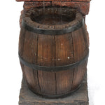 A wine barrel fountain with metal bands sits on a stone base, filled with water and soothing water sounds as gentle streams trickle in from above. LED lighting softly illuminates the scene for added ambiance.