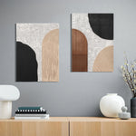 Two abstract art pieces with geometric shapes in black, brown, and beige adorn the gray wall, creating a personalized gallery wall above a wooden shelf. The setup includes books, a lamp, and decorative vases.