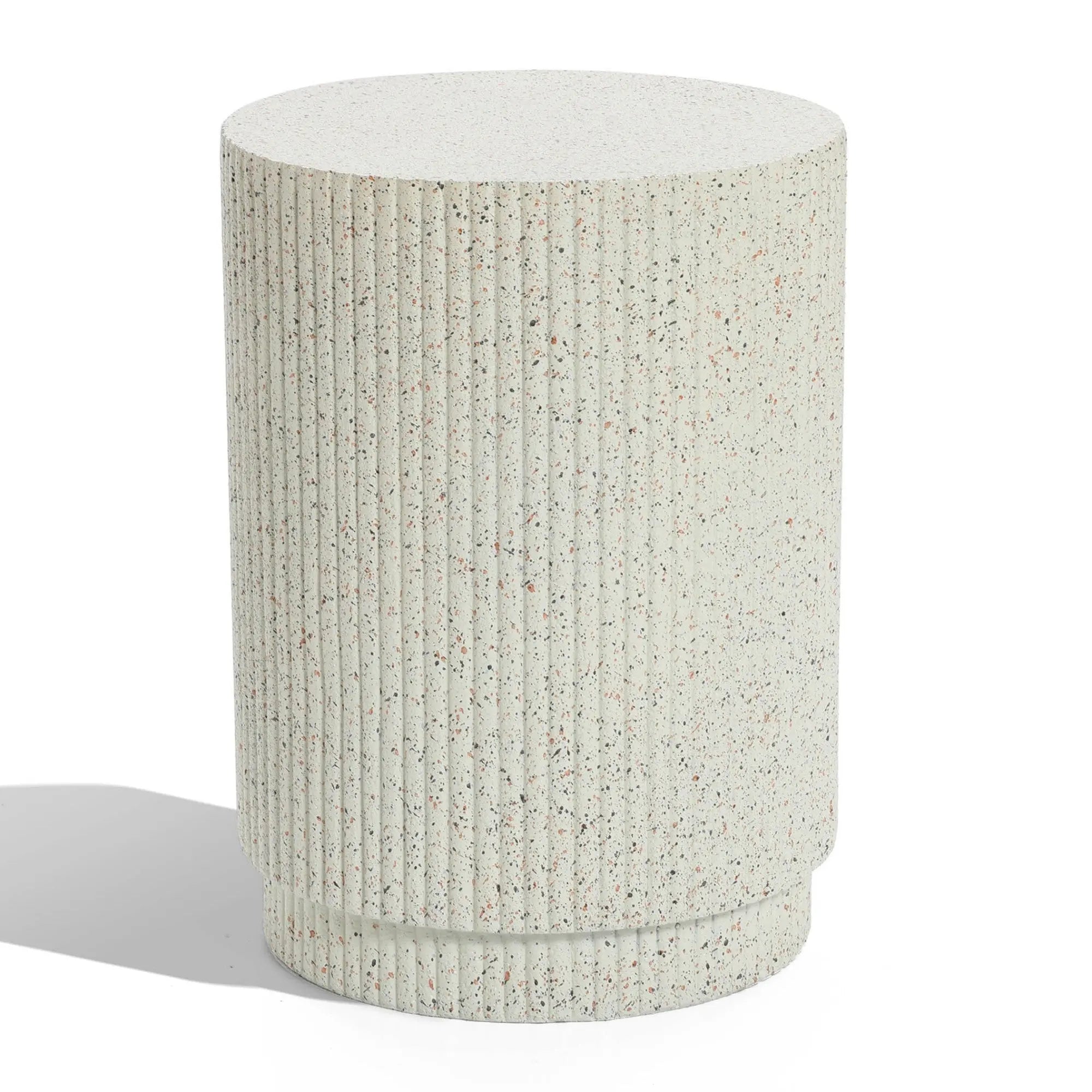 A textured, cylindrical, light-speckled concrete pedestal with vertical ridges stands on a flat surface, casting a shadow. This versatile table effortlessly blends function and style, offering an elegant touch to any space.