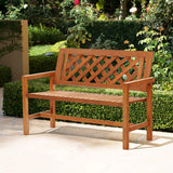 A solid wood garden bench with a lattice backrest adorns the stone patio, surrounded by lush green bushes and blooming roses.