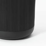 Close-up of a black cylindrical object with vertical ridges and a smooth base, resembling the sleek design of a stripes pattern planter, on a white background.