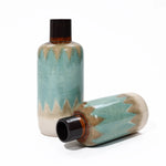 Two ceramic vases with a teal zigzag pattern exude nautical charm. One vase stands upright, while the other lies on its side, both showcasing a dark, narrow neck. Perfect tabletop decor for adding a coastal-inspired touch to any space.