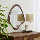 The Scandinavian charm shines through in the wood-framed wall mirror above a wooden dresser, adorned with books, a lidded jar, and a table lamp. A plant adds life to the minimalist design in the foreground.
