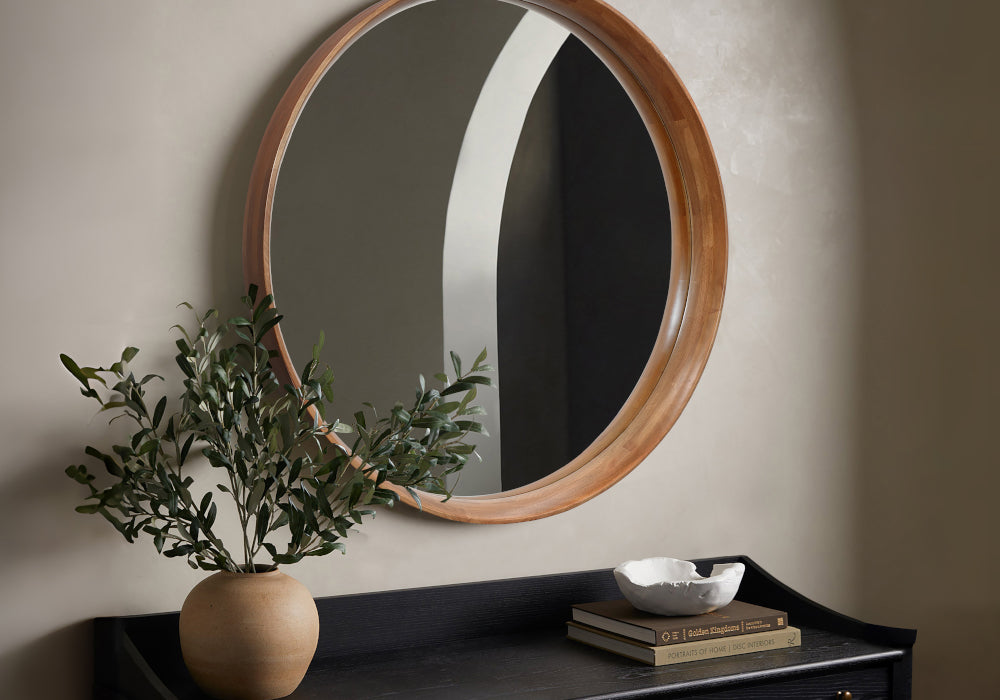 round wood frame accent mirror on the wall above black console table with terracotta vase on top