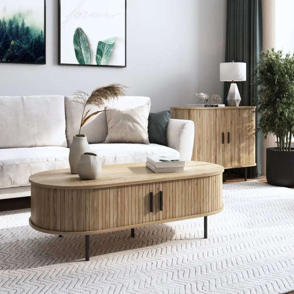 A modern living room with a beige sofa, a wooden coffee table, a side cabinet, potted plants, and framed wall art above the couch.