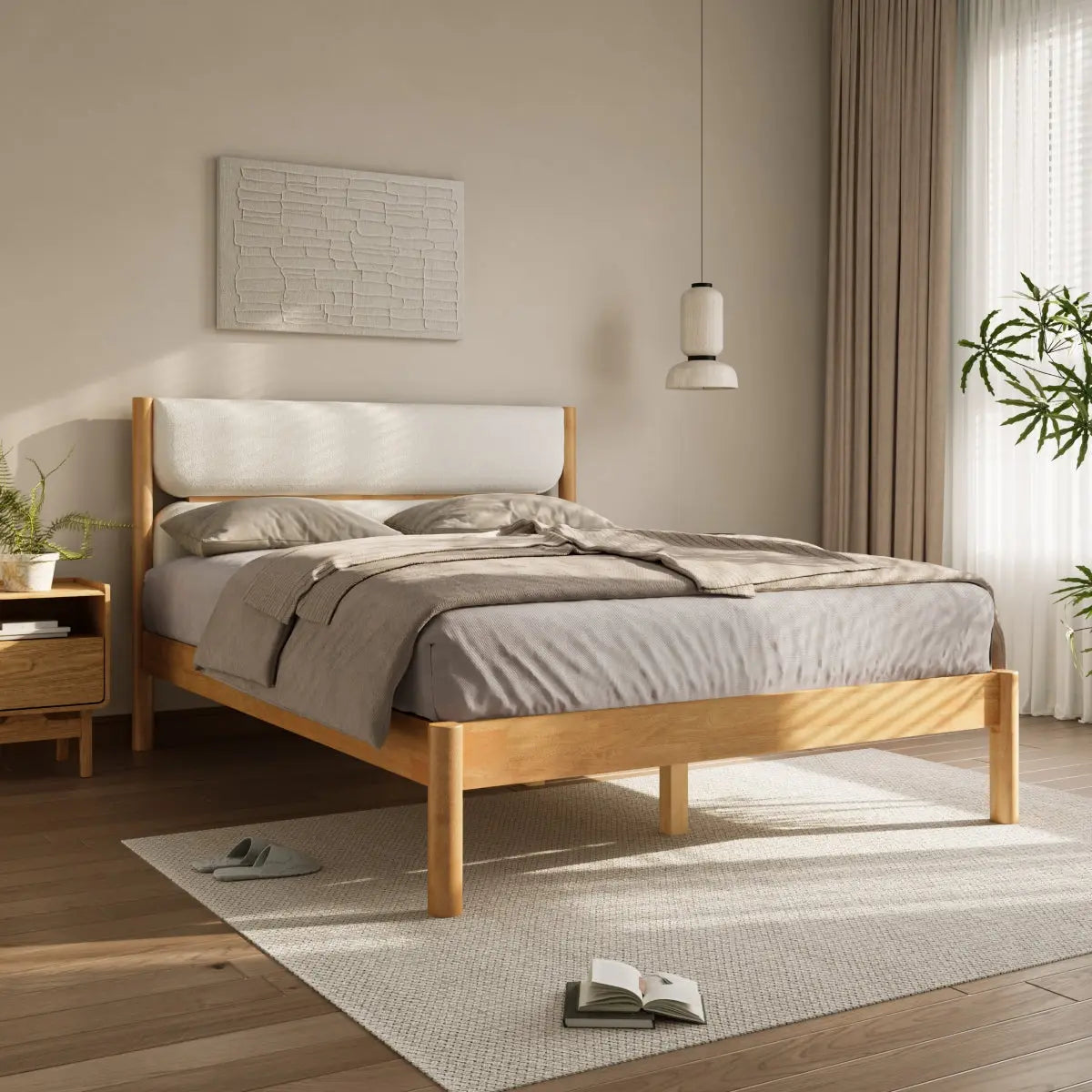 A neatly made bed with grey linens and a wooden frame stands in a sunlit bedroom. A small bedside table, plants, a hanging light, and an open book on the floor complete the decor.