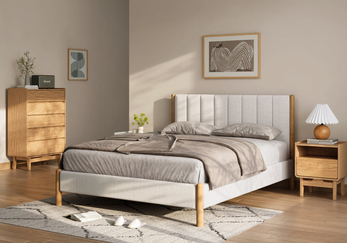 Minimalist bedroom with a wooden bed, gray bedding, a nightstand with a lamp, a dresser, wall art, and a light rug on a wooden floor.